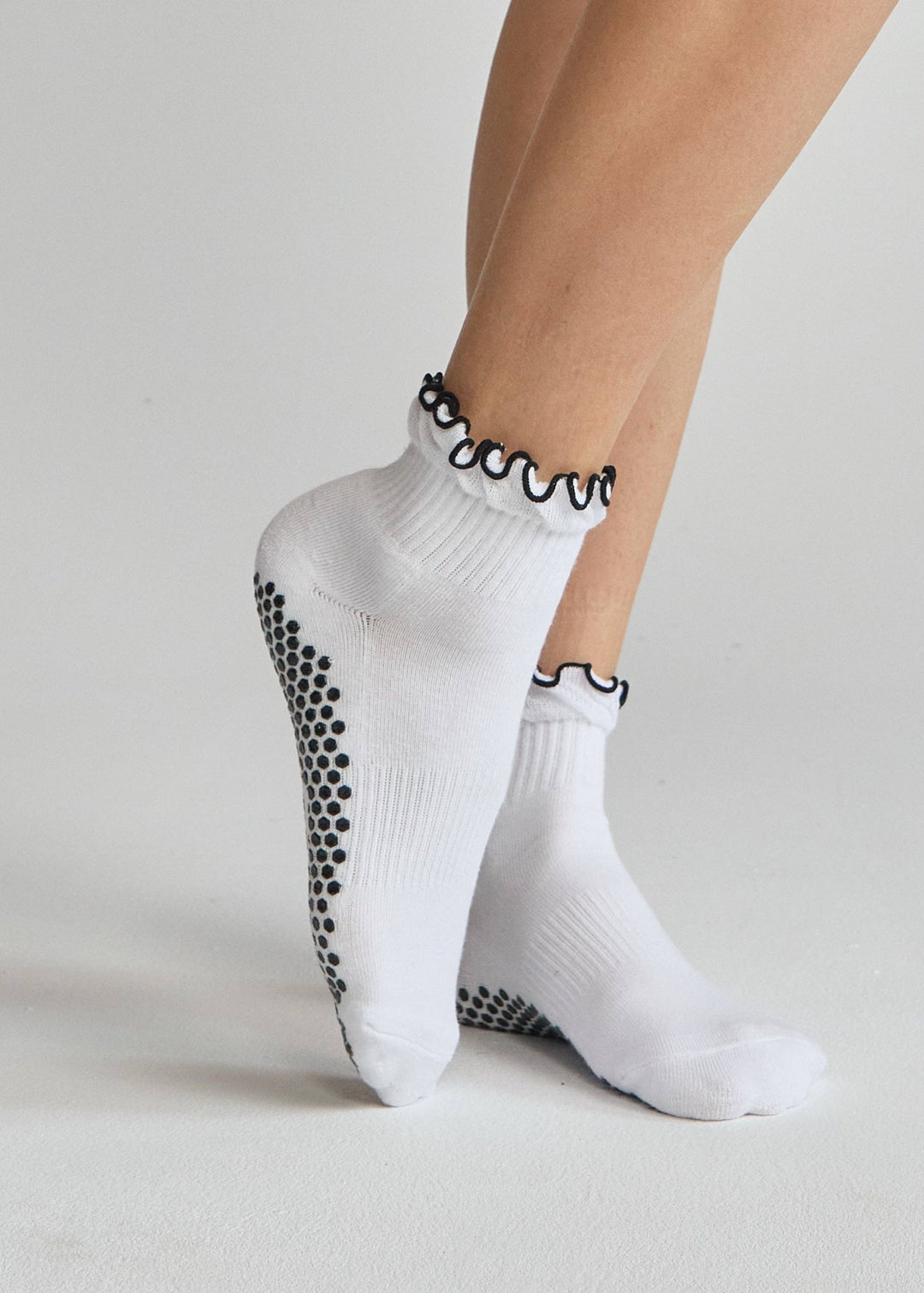 White socks with black grip dots worn by a person on a light gray background